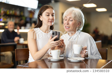 Elderly and young lady are having nice time in cafe, scrolling phone 134580310