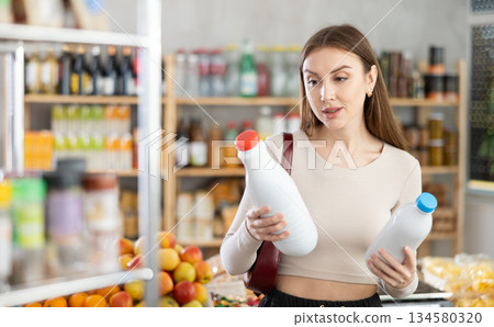 Girl hold packages bottles and choose consider milk in store Girl hold packages bottles and choose consider milk in store 134580320