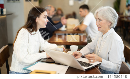 Elderly woman typing on laptop and communicating with young woman 134580348