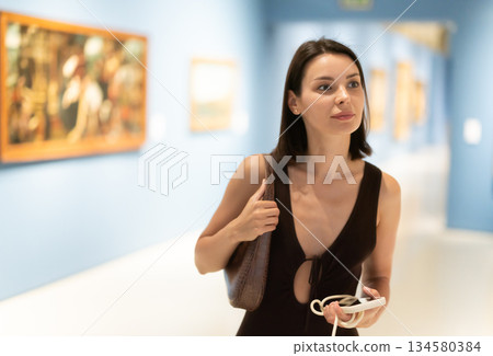 Young woman in summer clothes looking at paintings in museum 134580384