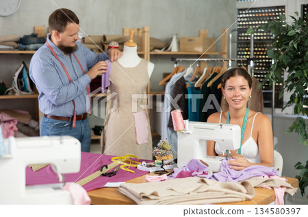Female dressmaker sewing at machine while colleague working with mannequin 134580397