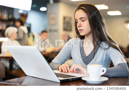 Young woman with laptop drinking coffee Young woman with laptop drinking coffee 134580408