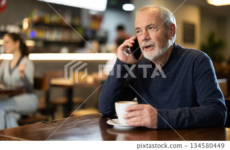Elderly man drinking coffee and talking on phone 134580449