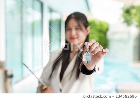 Real Estate Keys. A woman proudly holding house keys in front of a pool. 134582690