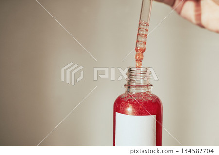 Person filling cosmetic dropper bottle with red serum Person filling cosmetic dropper bottle with red serum 134582704