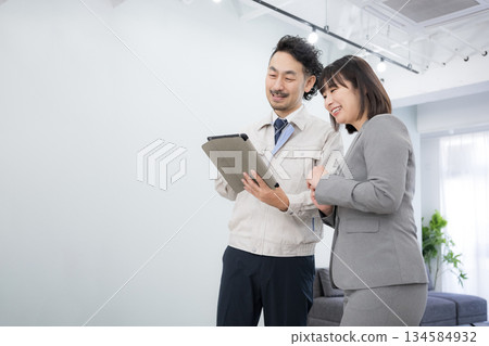 A man in work clothes and a woman in a suit check construction and interior estimates on a tablet A man in work clothes and a woman in a suit check construction and interior estimates on a tablet 134584932