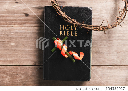 Crown of thorns with wooden cross, iron nail, ribbon on Bible, symbolizing Christian faith, sacrifice, crucifixion, Easter reflection, religious background for worship, prayer, devotion concepts Crown of thorns with wooden cross, iron nail, ribbon on Bible, symbolizing Christian faith, sacrifice, crucifixion, Easter reflection, religious background for worship, prayer, devotion concepts 134586927