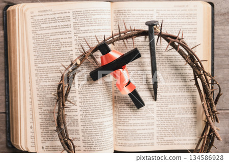 Crown of thorns with wooden cross, iron nail, ribbon on open Bible, symbolizing Christian faith, sacrifice, crucifixion, Easter reflection, religious background for worship, prayer, devotion concepts Crown of thorns with wooden cross, iron nail, ribbon on open Bible, symbolizing Christian faith, sacrifice, crucifixion, Easter reflection, religious background for worship, prayer, devotion concepts 134586928