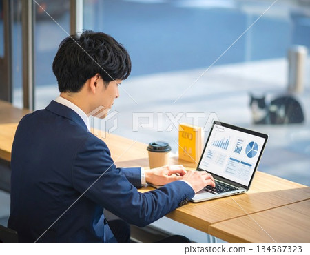 一個男人在咖啡館工作,一隻貓隨意地待在背景中。 一個男人在咖啡館工作,一隻貓隨意地待在背景中。 134587323