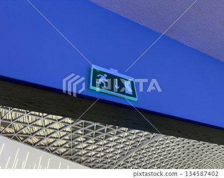 Green sign with reflective element depicting person running from building. Safe navigation in building during emergency or fire. Concept for rescuing and escaping burning building 134587402