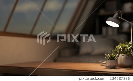 Wooden counter table with lamp and potted plant across sofa aside roof window in dim lit attic room Wooden counter table with lamp and potted plant across sofa aside roof window in dim lit attic room 134587886