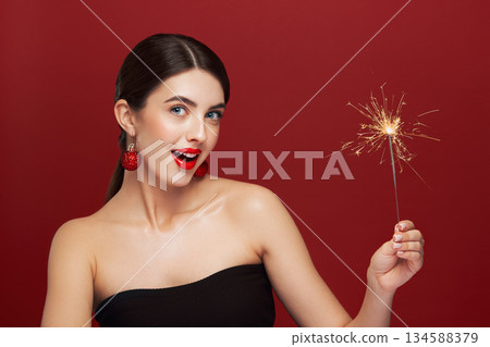 Beautiful young woman holds a sparkler on red background 134588379