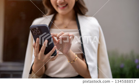 Close up of a woman's hands holding and touching on the smartphone while walking around the building Close up of a woman's hands holding and touching on the smartphone while walking around the building 134588857
