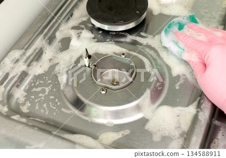 Hand in rubber glove cleaning stainless steel gas stove with sponge and soap foam. Cleaning concept. 134588911