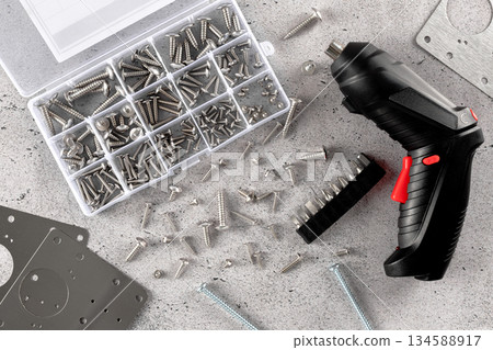 Electric screwdriver with set of metal screws drill bits on workshop table. DIY repair tools concept Electric screwdriver with set of metal screws drill bits on workshop table. DIY repair tools concept 134588917