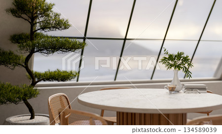 Coffee cup and books on grey marble table with wooden chair next to potted bonsai under roof window. 134589039