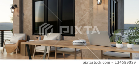 Laptop on wooden table with books and potted plants at balcony or terrace of a brown painted house. 134589059