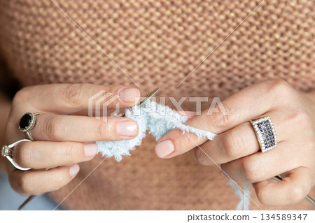 Woman Knitting with White Yarn Close-Up. A woman knit with knitting needles,closeup shot 134589347