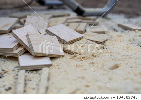 Pile of wooden cutoffs and sawdust scattered on a workshop floor, showcasing craftsmanship and the process of woodworking in a creative environment with tools nearby 134589743