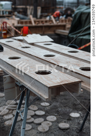Wooden workbench with circular cutouts, surrounded by construction materials and tools, showcasing craftsmanship and industrial workspace atmosphere in a busy workshop environment Wooden workbench with circular cutouts, surrounded by construction materials and tools, showcasing craftsmanship and industrial workspace atmosphere in a busy workshop environment 134589749