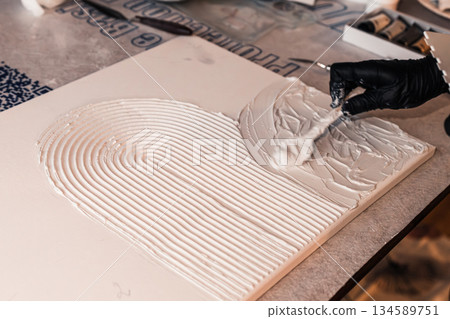 Artist applying textured white paste on canvas with a spatula, creating a unique abstract design, showcasing creativity and craftsmanship in modern art 134589751