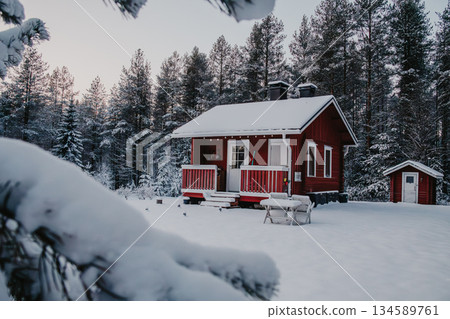 Cozy red cabin nestled in a snowy landscape surrounded by tall evergreen trees, creating a serene winter atmosphere with soft sunlight filtering through branches Cozy red cabin nestled in a snowy landscape surrounded by tall evergreen trees, creating a serene winter atmosphere with soft sunlight filtering through branches 134589761
