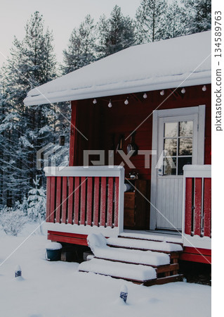 Cozy red cabin in winter landscape, surrounded by snow-covered trees, features a welcoming porch with snow on steps, creating a serene and inviting atmosphere for relaxation Cozy red cabin in winter landscape, surrounded by snow-covered trees, features a welcoming porch with snow on steps, creating a serene and inviting atmosphere for relaxation 134589763