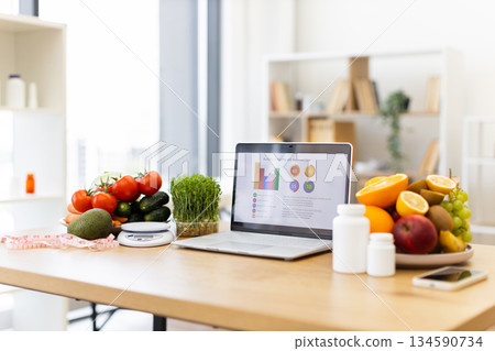 A laptop displays a diet plan next to a plate of fruits and vegetables, promoting healthy eating habits. 134590734