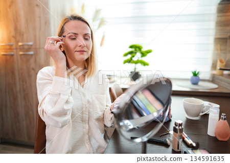 Woman applying makeup in bright, stylish home environment 134591635