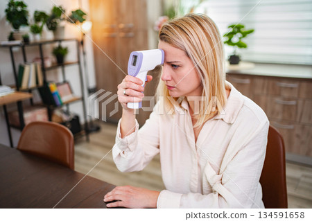 Woman checks her temperature with a digital thermometer at home 134591658