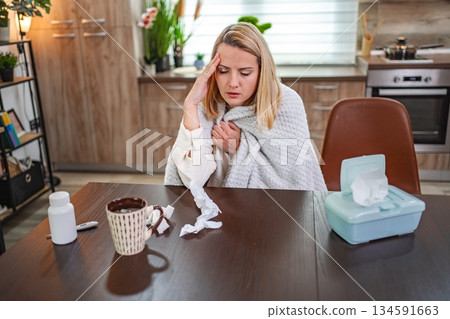 Feeling unwell at home while wrapped in a blanket and sipping tea Feeling unwell at home while wrapped in a blanket and sipping tea 134591663