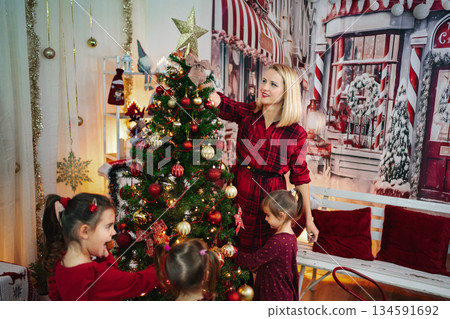 Mother and children decorating Christmas tree for holiday celebration Mother and children decorating Christmas tree for holiday celebration 134591692