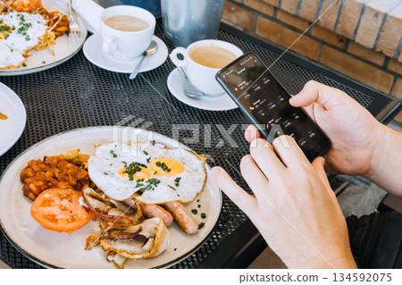 Hands hold smartphone displaying food tracking application over breakfast plate. Nutrition tracking, calorie counter app, digital health, healthy lifestyle technology. Hands hold smartphone displaying food tracking application over breakfast plate. Nutrition tracking, calorie counter app, digital health, healthy lifestyle technology. 134592075