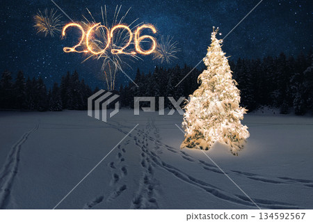 Magical New Year 2026 winter scene. brightly lit, snowy Christmas tree stands under a starry night sky with the year 2026 drawn in golden sparkler light above a dark forest and fresh footprints. Snow 134592567