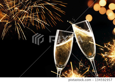 Two champagne flutes clinking on a night sky with golden fireworks, sparklers, and soft bokeh lights 134592957