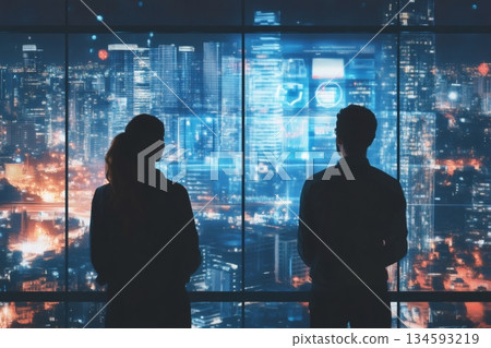Two businesspeople looking out large windows at a futuristic cityscape with holographic graphs and data displayed over the buildings 134593219