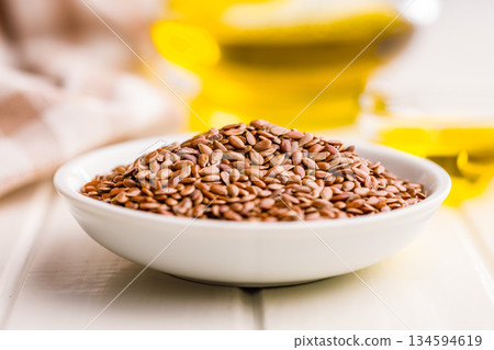 Brown linseed or flaxseed and oil. Healthy flax seed in bowl on white table. 134594619