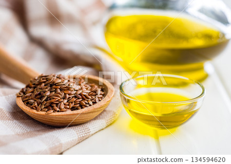 Brown linseed or flaxseed and oil. Healthy flax seed on wooden spoon on white table. Brown linseed or flaxseed and oil. Healthy flax seed on wooden spoon on white table. 134594620
