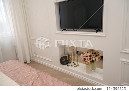 Bedroom interior, white decorative wall with TV, clock, vase with flowers. 134594825