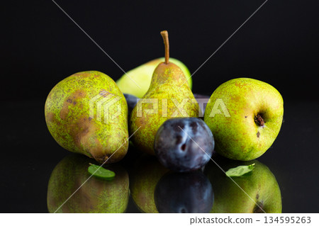 Ripe pears and plums on a black background Ripe pears and plums on a black background 134595263