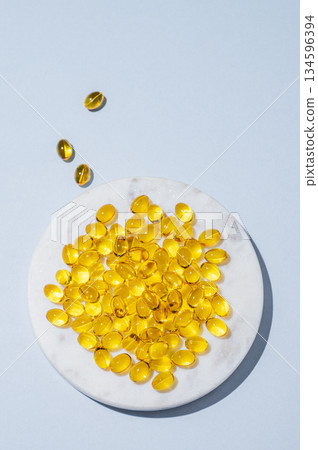 Yellow softgel vitamins capsules on a white marble plate on a blue background with shadow Yellow softgel vitamins capsules on a white marble plate on a blue background with shadow 134596394