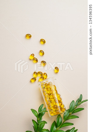 Yellow softgel vitamins capsules scattered in a bottle on a light background with green leaf. Yellow softgel vitamins capsules scattered in a bottle on a light background with green leaf. 134596395