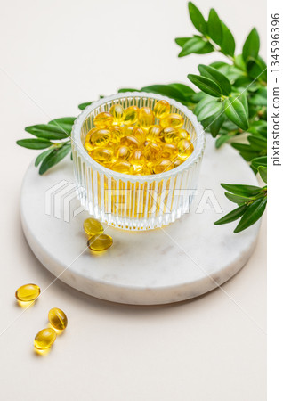 Yellow softgel vitamins capsules in a bowl on a marble stand on a light background 134596396