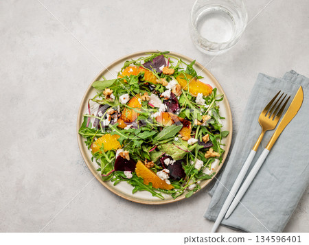 A fresh salad of beets, orange, and arugula with feta, walnuts, and balsamic dressing on a plate 134596401