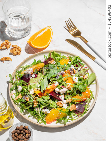 A fresh salad of beets, orange, and arugula with feta, walnuts, and balsamic dressing on a plate 134596402