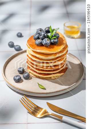 Pancakes with blueberry on a plate on a light tile background with morning shadows,  honey 134596410