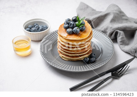 Stack of pancakes with fresh blueberries and suryp on a gray plate on a light background 134596423