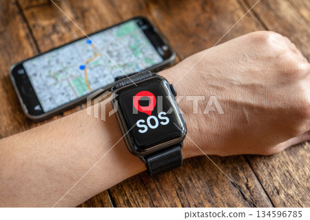 hand with a smartwatch holds a mobile phone. The phone screen shows a navigation map with a prominent red emergency. 134596785