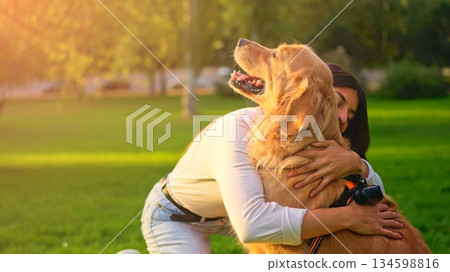 Woman hugging golden retriever dog in park at sunset 134598816