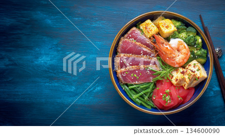 The bowl, holding a diverse array of fresh ingredients, is positioned on the right, with dark wooden chopsticks resting beside it 134600090